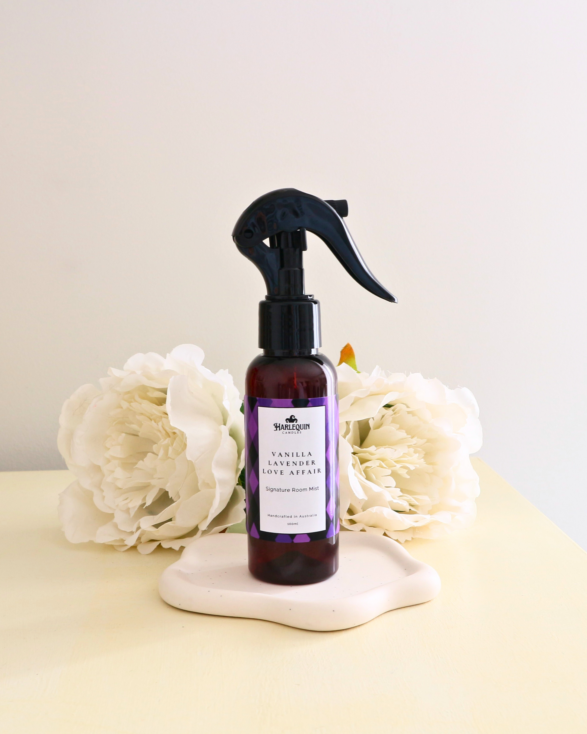 Handcrafted Australian Vanilla Lavender room mist by Harlequin Candles, presented in a luxe amber spray bottle on a textured woven mat against a soft neutral background.
