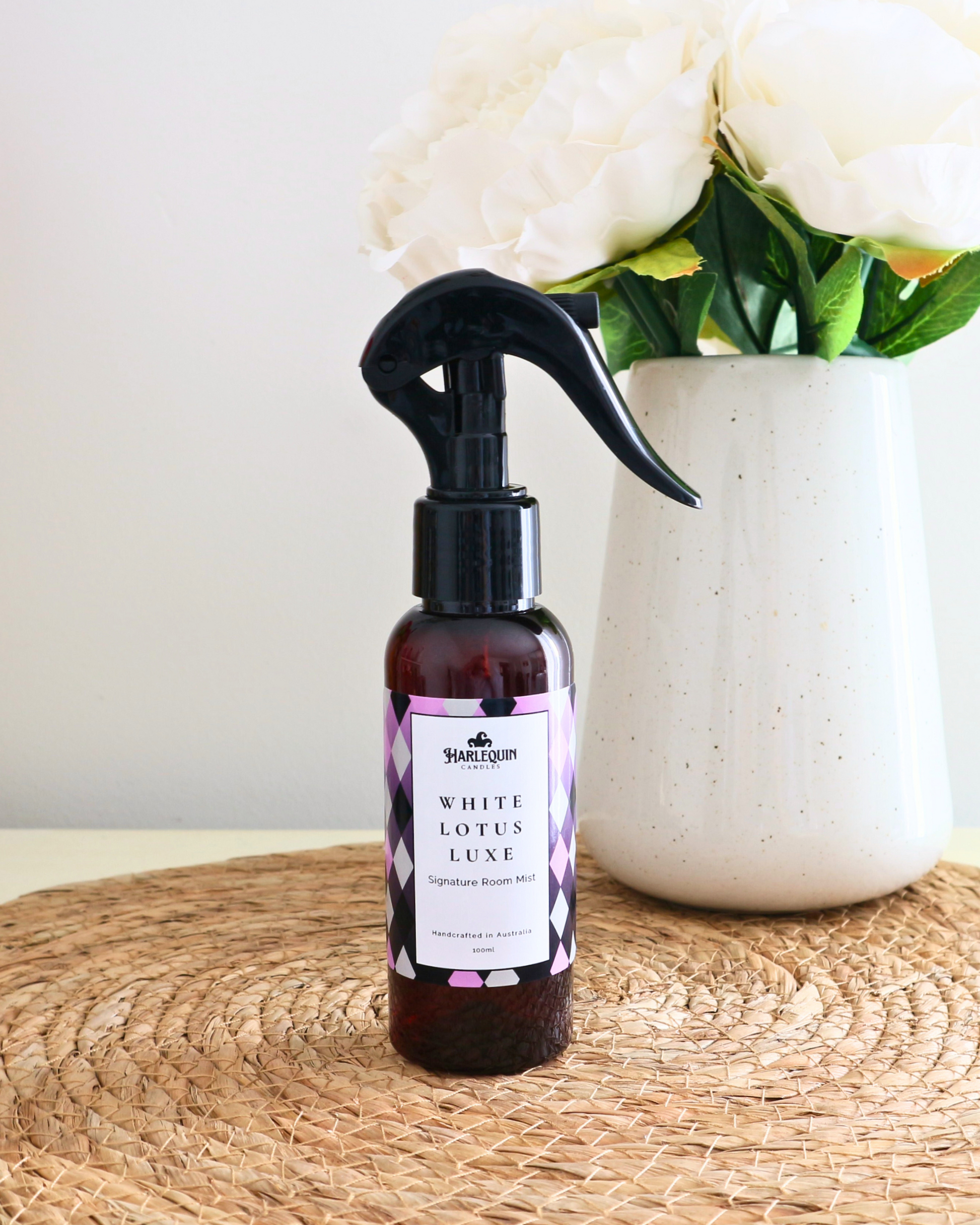Handcrafted Australian white lotus room mist by Harlequin Candles, presented in a luxe amber spray bottle on a textured woven mat against a soft neutral background.