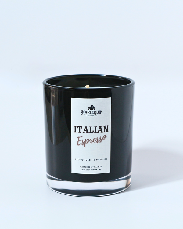 A Harlequin Candles "Italian Espresso" hand-poured soy wax candle in a black glass jar, resting on a blue book. Premium Australian made scented candle.