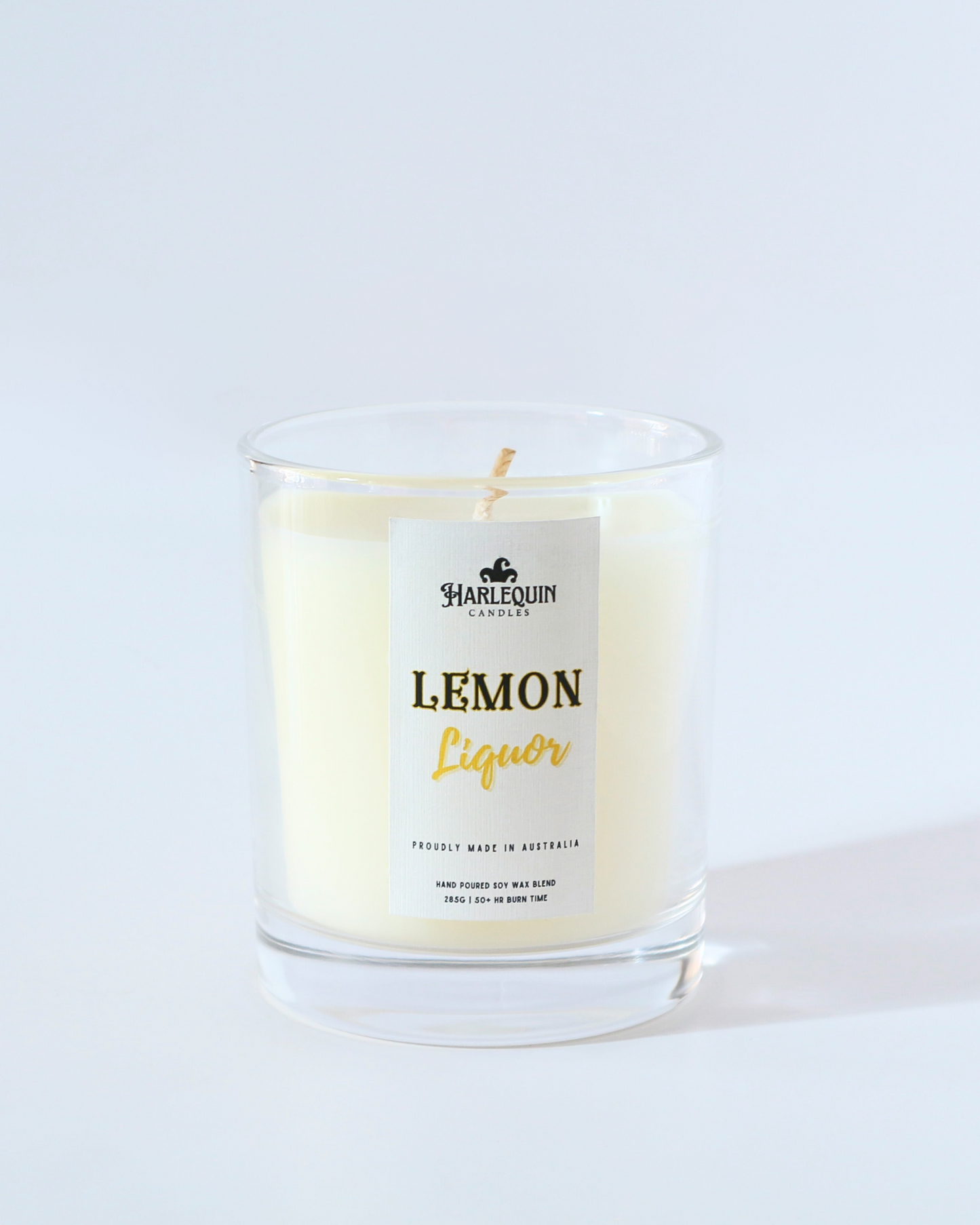 A Harlequin Candles "Lemon Liquor" hand-poured soy wax candle in a clear glass jar, styled on a wooden tray next to a potted succulent plant. Premium Australian made scented candle.