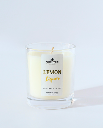 A Harlequin Candles "Lemon Liquor" hand-poured soy wax candle in a clear glass jar, styled on a wooden tray next to a potted succulent plant. Premium Australian made scented candle.