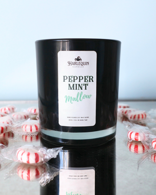A Harlequin Candles "Peppermint Mallow" hand-poured soy wax candle in a black glass jar, surrounded by individually wrapped peppermint lollies on a reflective surface. Premium Australian made scented candle.