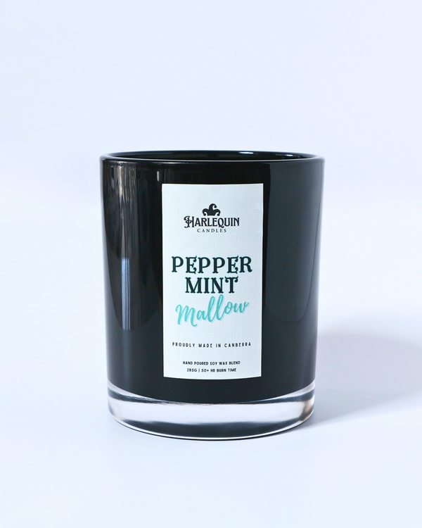 A Harlequin Candles "Peppermint Mallow" hand-poured soy wax candle in a black glass jar, surrounded by individually wrapped peppermint lollies on a reflective surface. Premium Australian made scented candle.