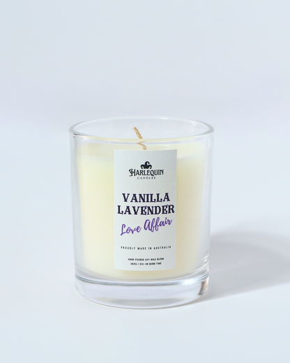 A Harlequin Candles "Vanilla Lavender Love Affair" hand-poured soy wax candle in a clear glass jar, presented on a wooden tray with pink tulips. Premium Australian made scented candle.