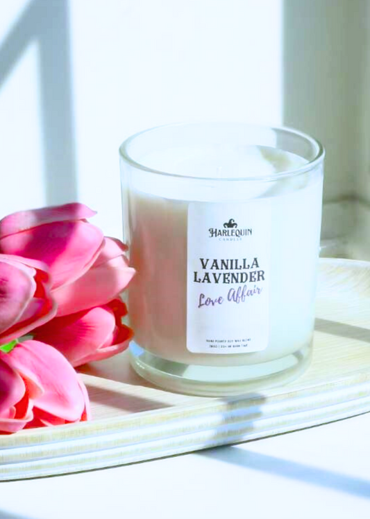 A Harlequin Candles "Vanilla Lavender Love Affair" hand-poured soy wax candle in a clear glass jar, presented on a wooden tray with pink tulips. Premium Australian made scented candle.