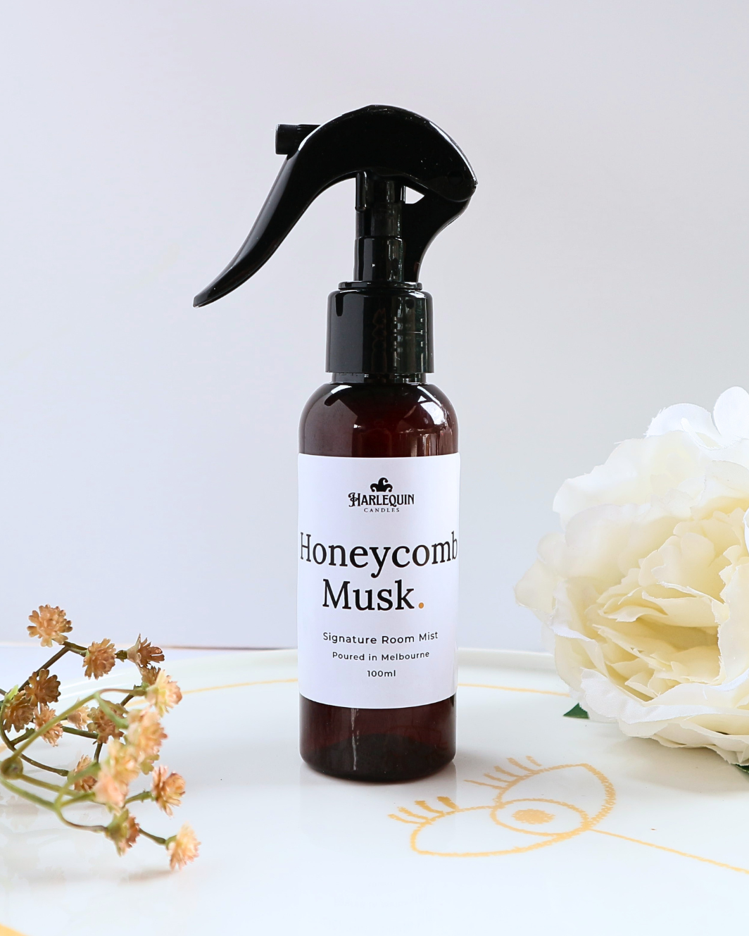 Luxury Honeycomb Musk home fragrance spray styled with a white peony flower and dried botanicals on a designer ceramic tray, warm and sweet room deodorizer by Harlequin Candles.