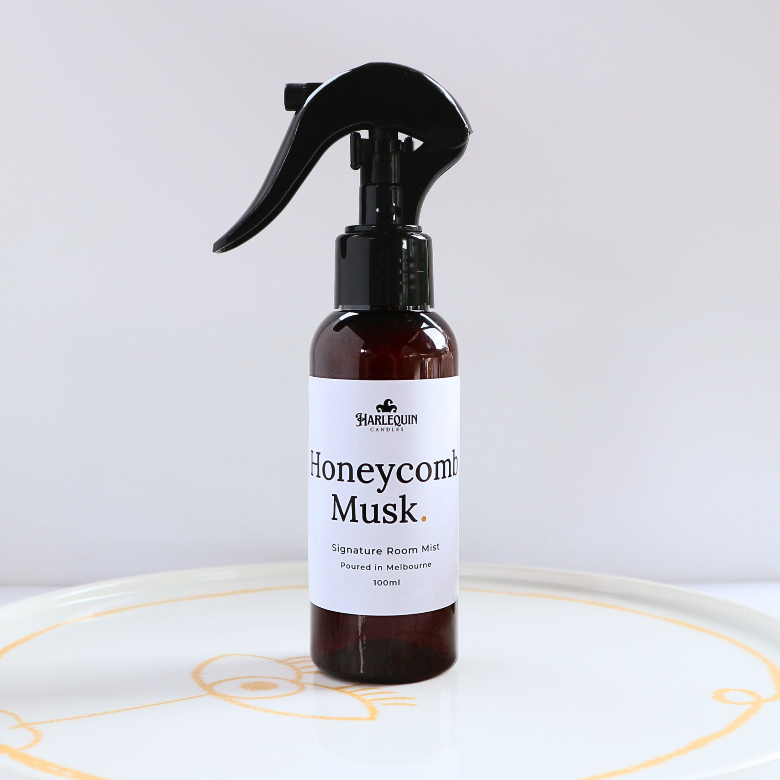Harlequin Candles Honeycomb Musk 100ml signature room mist in a premium amber spray bottle on a minimalist white ceramic tray, hand-poured in Melbourne Australia.