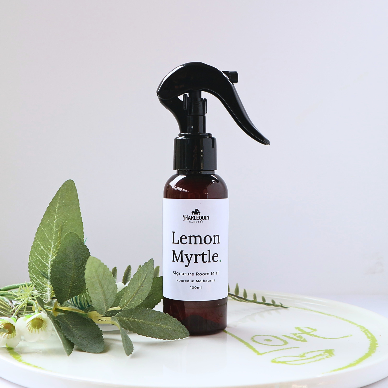 Luxury Lemon Myrtle home fragrance spray styled with fresh green eucalyptus leaves on a white designer tray, refreshing Australian native room deodorizer by Harlequin Candles.