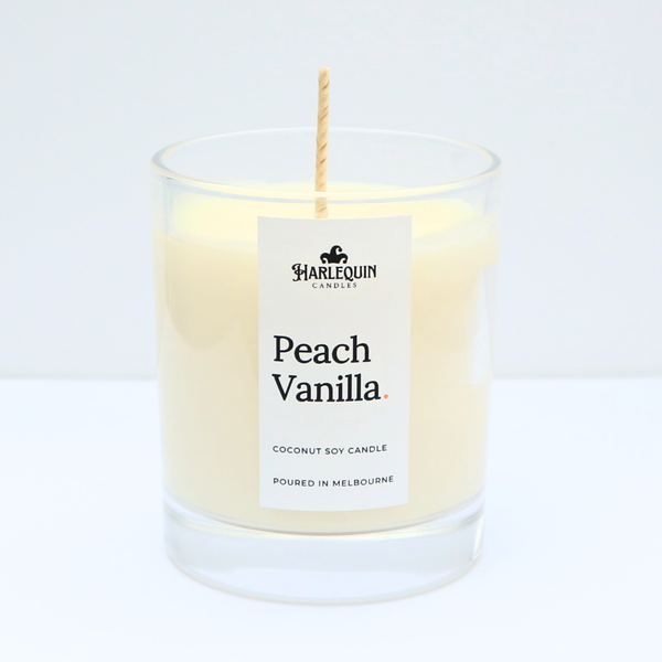 A close-up of a Peach Vanilla coconut soy candle by Harlequin Candles in a clear glass jar. The minimalist white label features the brand's logo and the text "Poured in Melbourne" against a clean white background.
