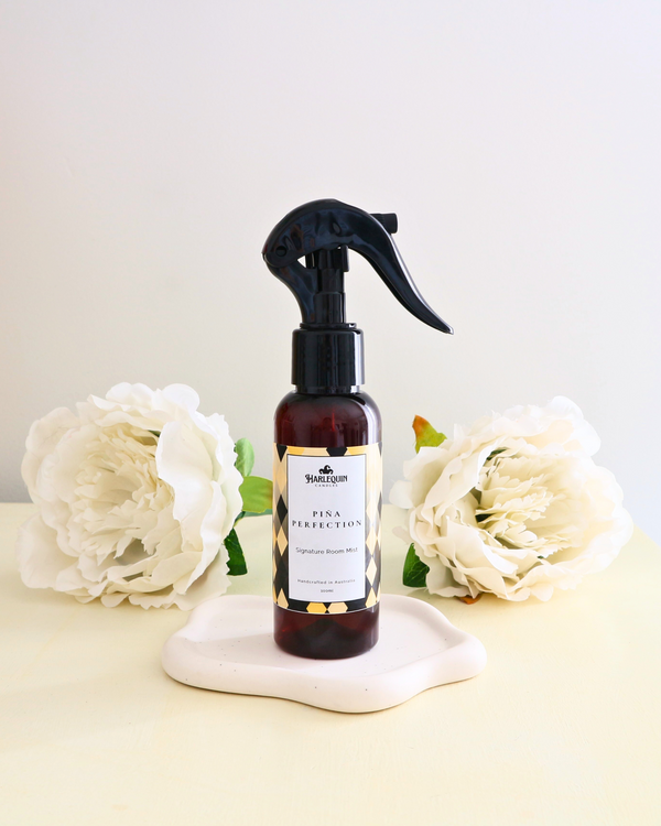 Handcrafted Australian pina colada room mist by Harlequin Fragrance, presented in a luxe amber spray bottle on a textured woven mat against a soft neutral background.