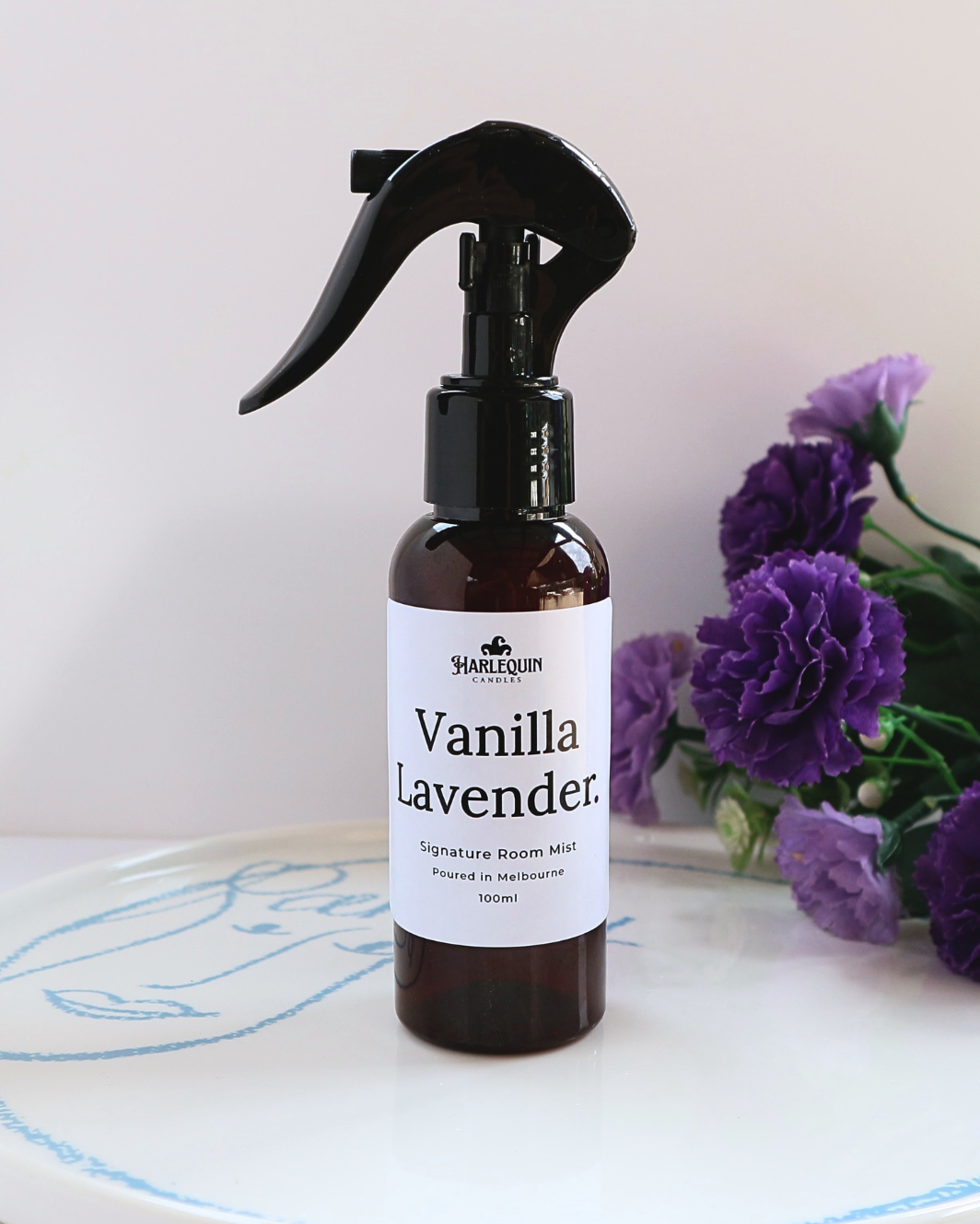 Luxury Vanilla Lavender home fragrance spray styled with purple carnations on a white designer tray, relaxing aromatherapy mist and linen spray by Harlequin Candles.