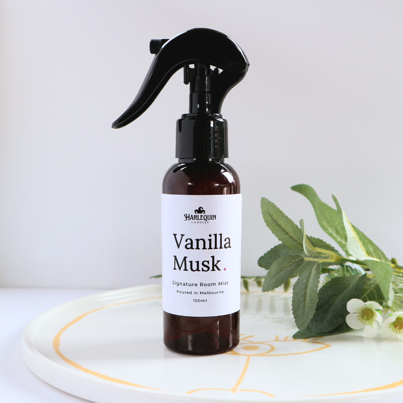 Luxury Vanilla Musk home fragrance spray styled with green botanical leaves on a white designer tray, sophisticated room deodorizer and aromatherapy mist by Harlequin Candles.