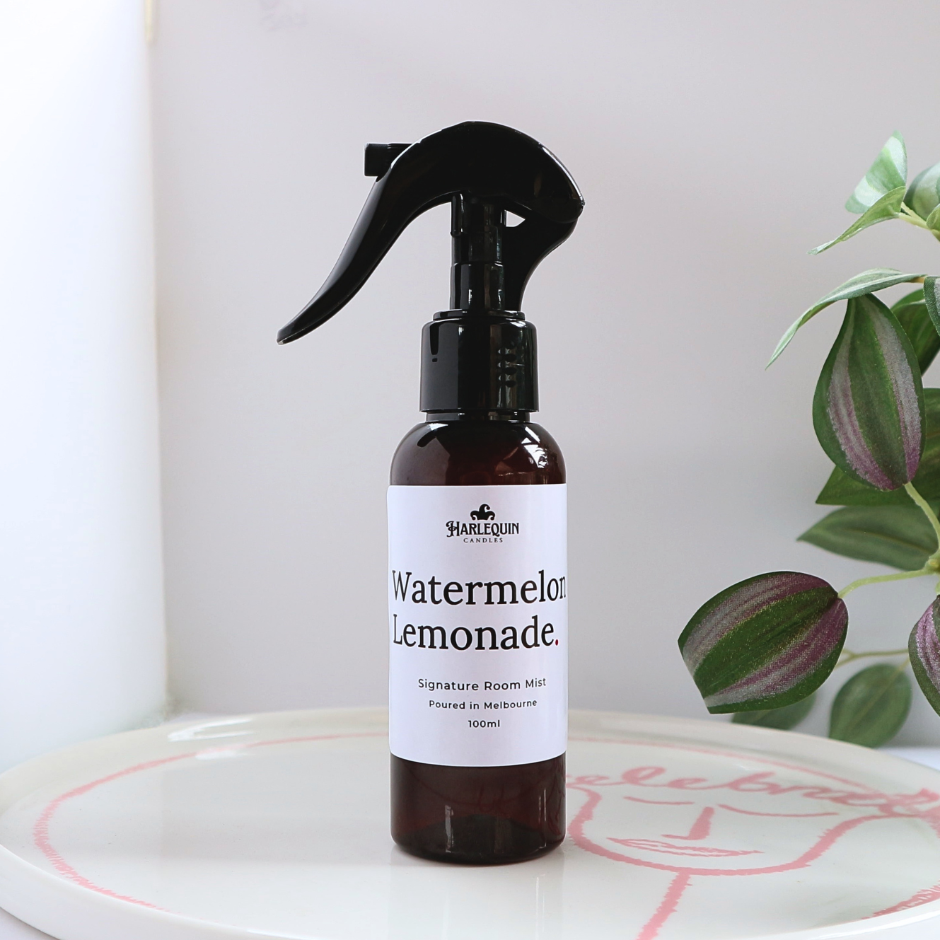 Luxury Watermelon Lemonade home fragrance spray styled with green leaves on a white designer tray, refreshing sweet room deodorizer and aromatherapy mist by Harlequin Candles.