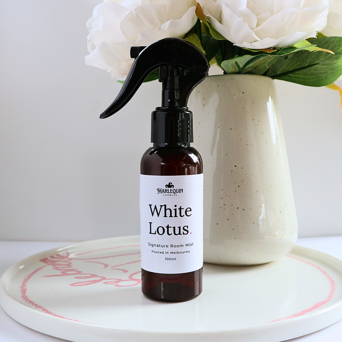 Luxury White Lotus home fragrance spray styled with white peony flowers in a ceramic vase, elegant floral room deodorizer by Harlequin Candles.